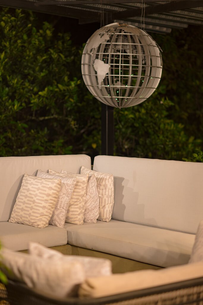 Zona lounge con sofá en L, cojines decorativos y lámpara colgante en eco lodge Rivabella, Boyacá.